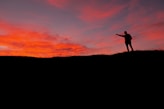 A silhouette of a person standing on a hill at sunset.