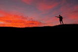 A silhouette of a person standing on a hill at sunset.