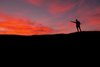 A sunset silhouette of a person standing tall on a hill, symbolizing gratitude and perseverance.