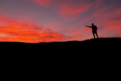 A silhouette of a person standing on a hill at sunset.