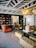 An elegant and stylish living room features a geometric patterned floor, leather sofas, and a central black table. Bookshelves line one wall, while a modern chandelier illuminates the space. Decorative plants and candles add a touch of nature and coziness.
