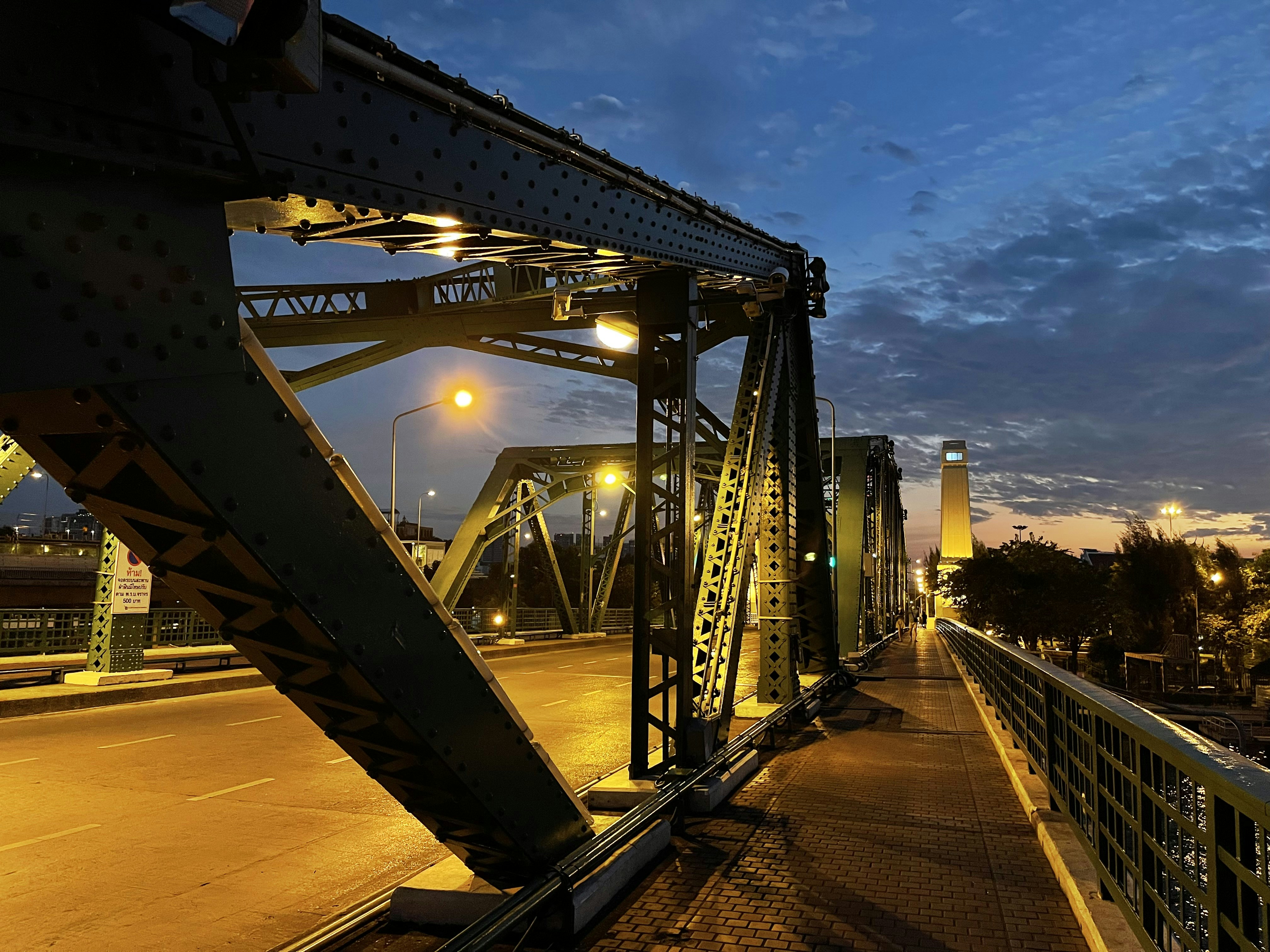 Weathering steel pedestrian bridge over harbour water at dusk with warm amber light reflections