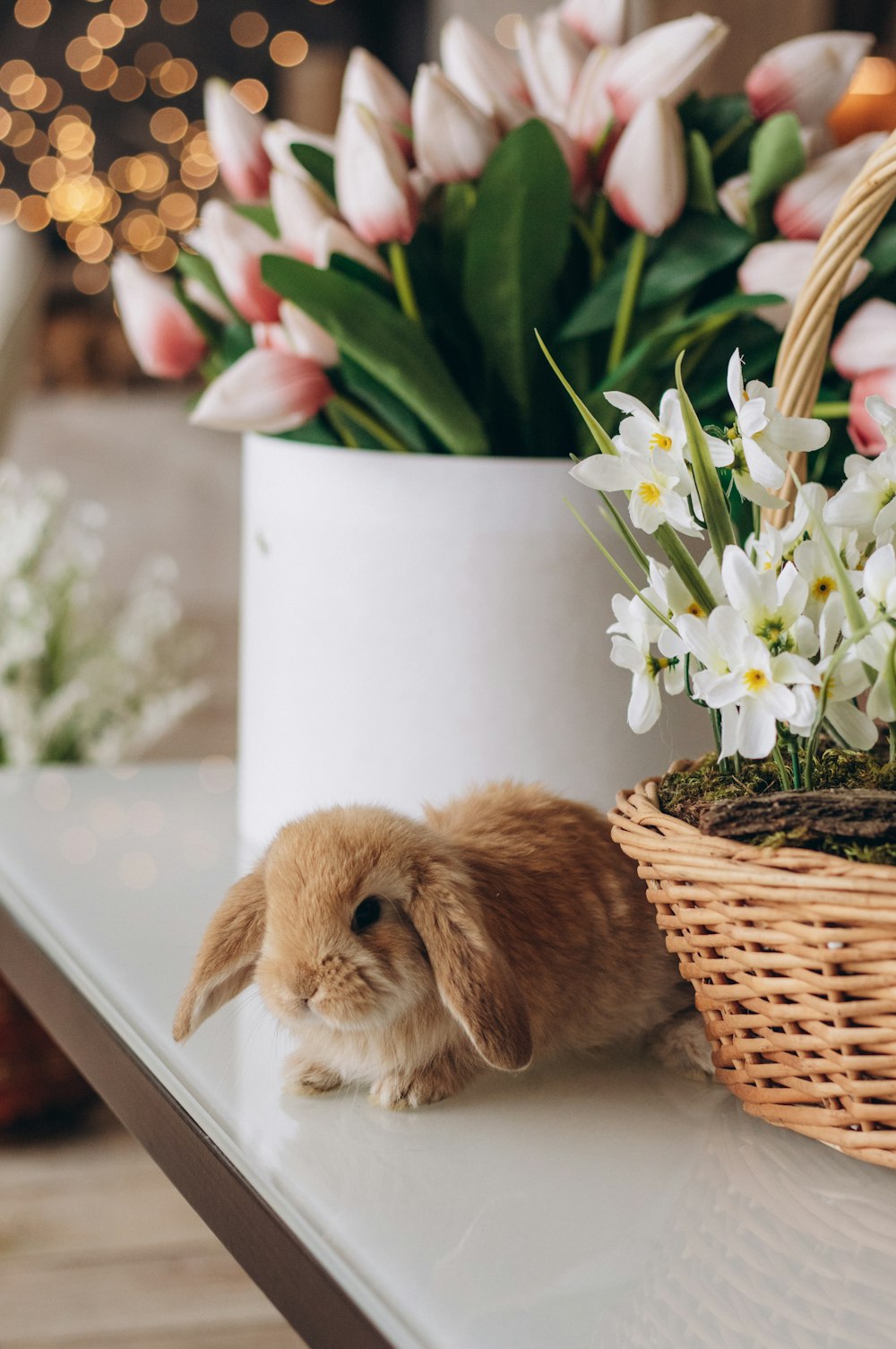 a small rabbit sitting on a table next to a basket of flowers