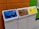 Three recycling bins are lined up next to each other against a colorful wall. The bins are labeled for different materials: paper with a blue top, plastic with a brown top, and aluminum with a yellow top. Each bin has a distinct shape for the deposit slot appropriate for the material.