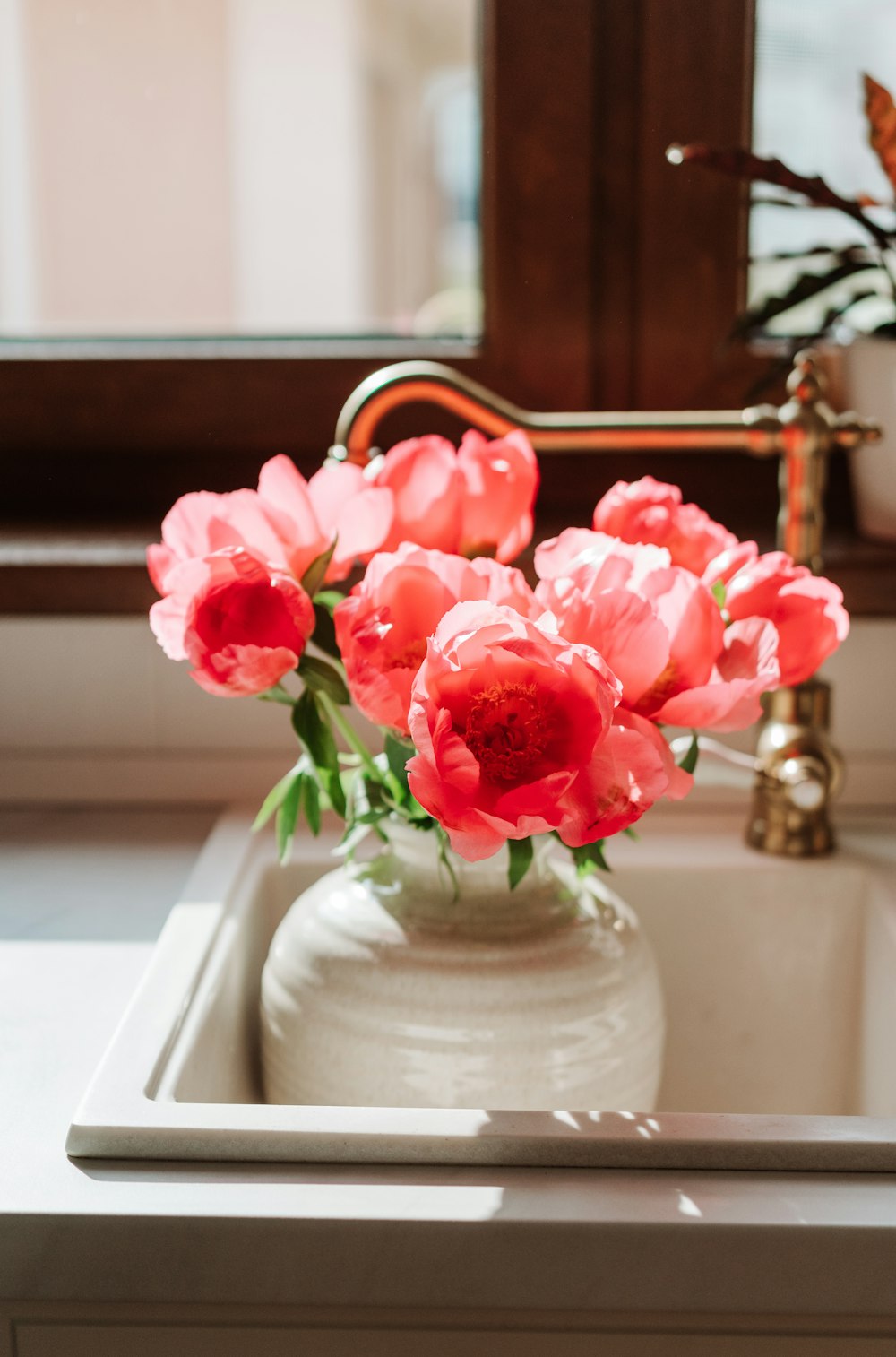 a white vase filled with pink flowers on top of a sink