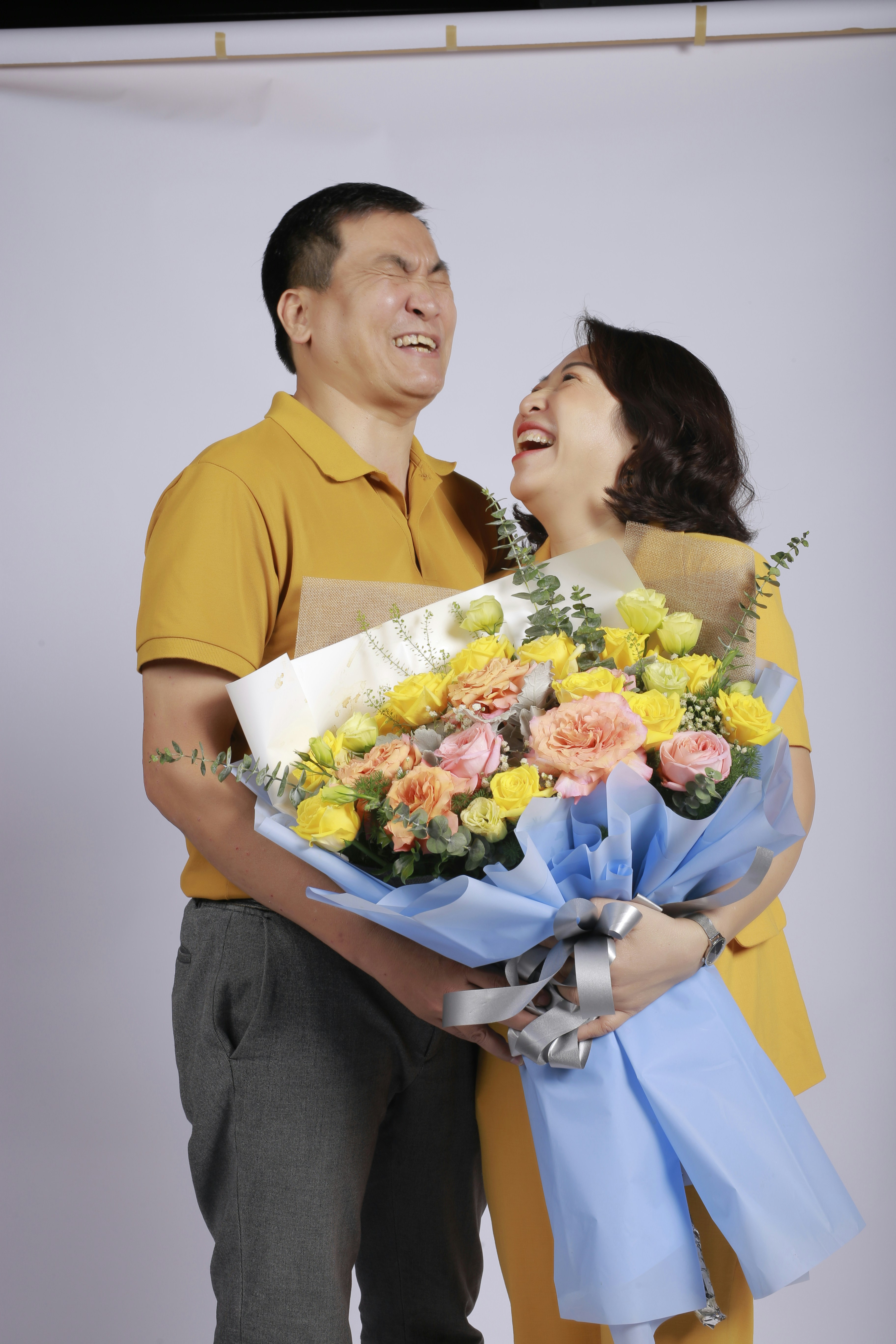 Couple sharing a joyful laugh in a garden full of blooming pink flowers, bright daylight, candid happiness