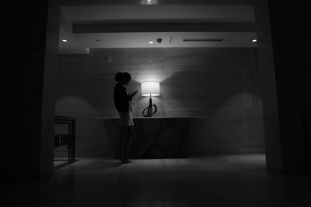 a woman standing in a dark room next to a lamp