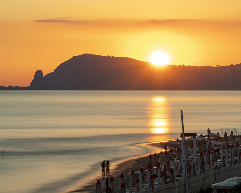 the sun is setting over a beach with umbrellas