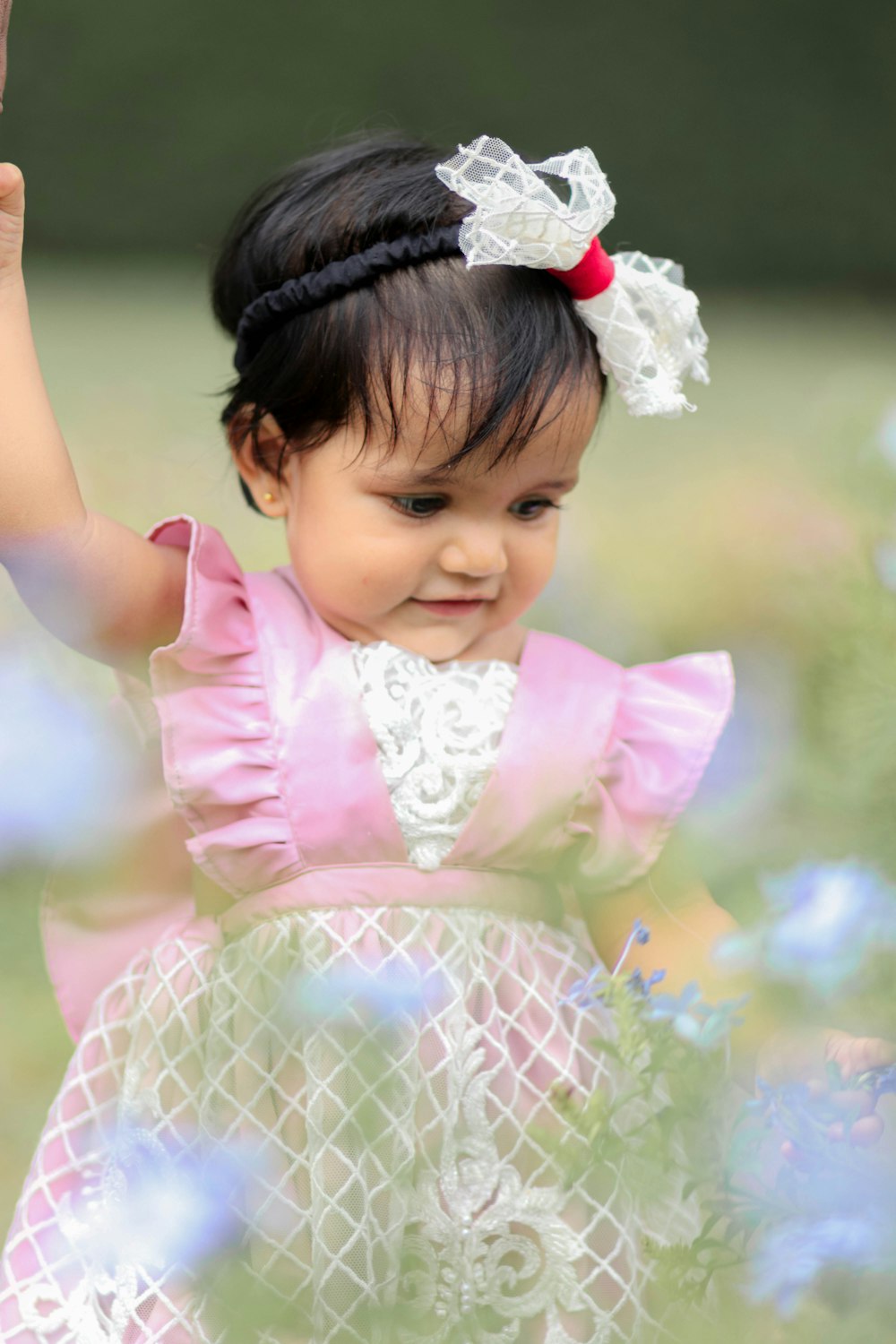 a little girl in a pink dress holding her hand up