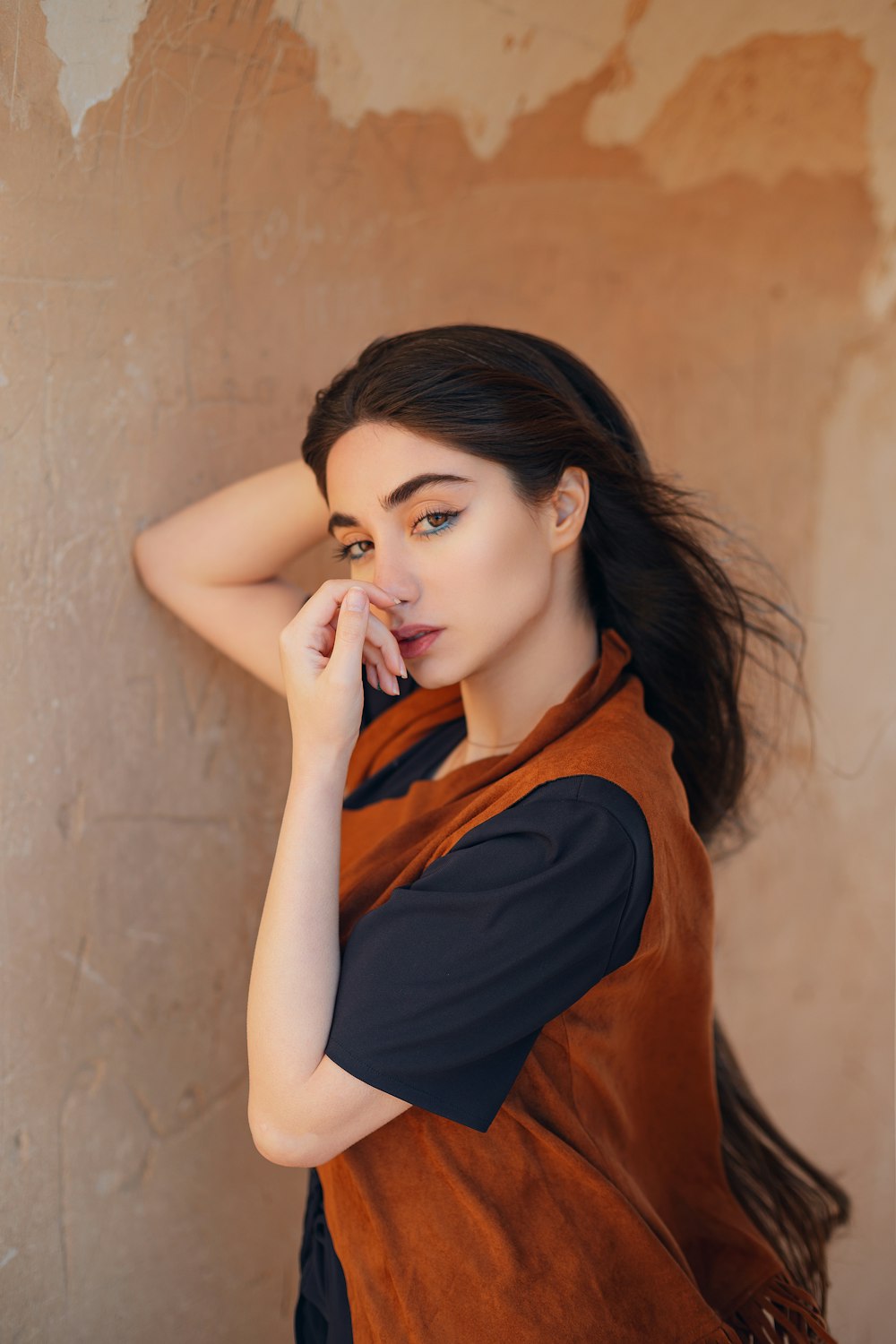 a woman leaning against a wall with her hand on her face