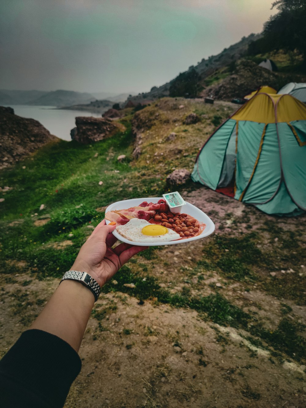 a person holding a plate of food in front of a tent
