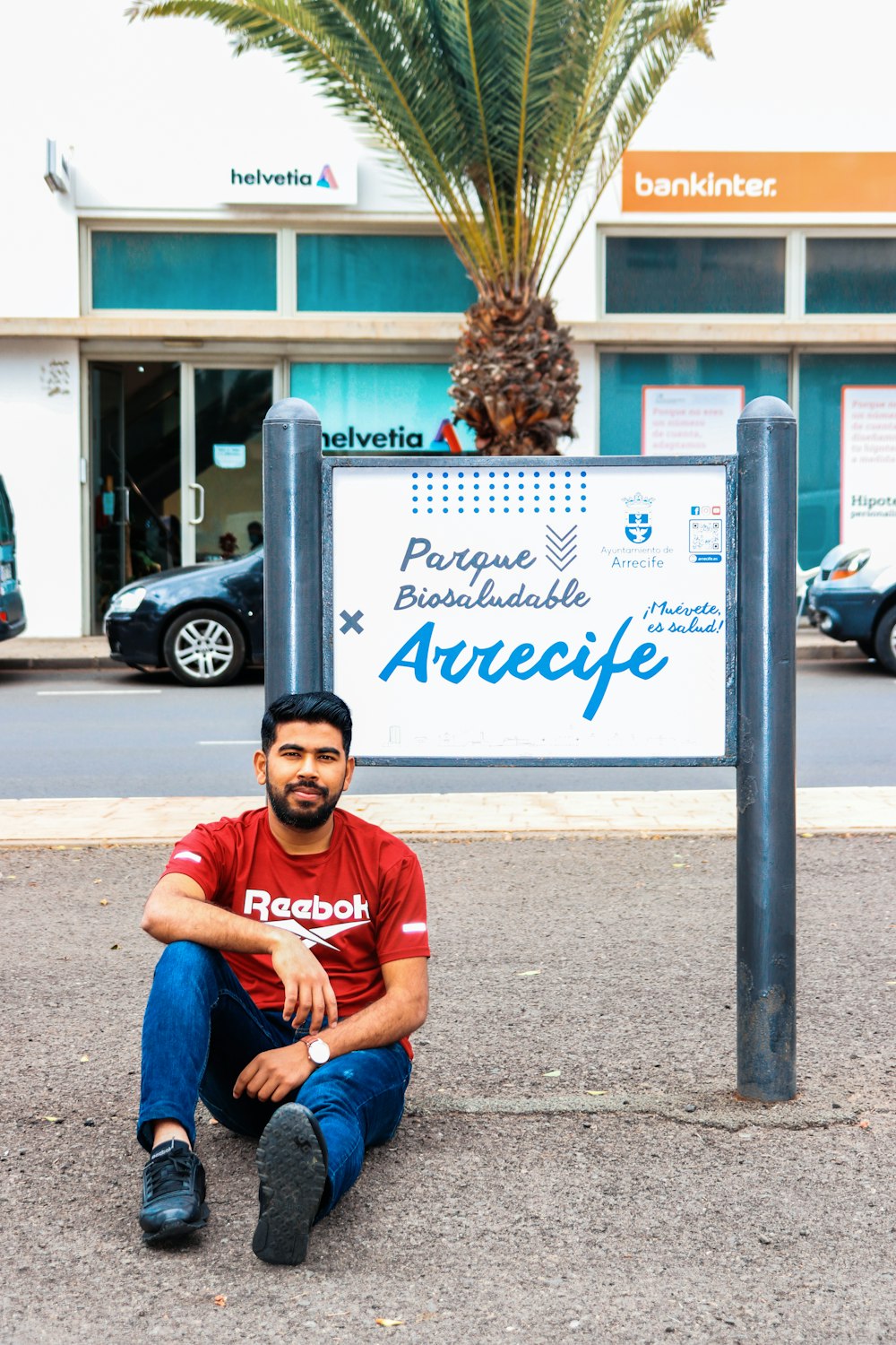 a man sitting on the ground next to a palm tree