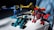 Three colorful toy robots are positioned on a white surface. The robots are constructed with interlocking plastic pieces in blue, yellow, and red colors. Sunlight casts shadows, adding depth to the scene, and a blue curtain is visible in the background.