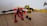 Two toy robots feature prominently, crafted from colorful plastic pieces. One is predominantly red and black, with a shield-like emblem on its chest and a small fire piece in its hand. The other is primarily yellow and black, with extended arms resembling mechanical forks. They stand on a wooden floor with a white wall and part of a door hinge visible in the background.