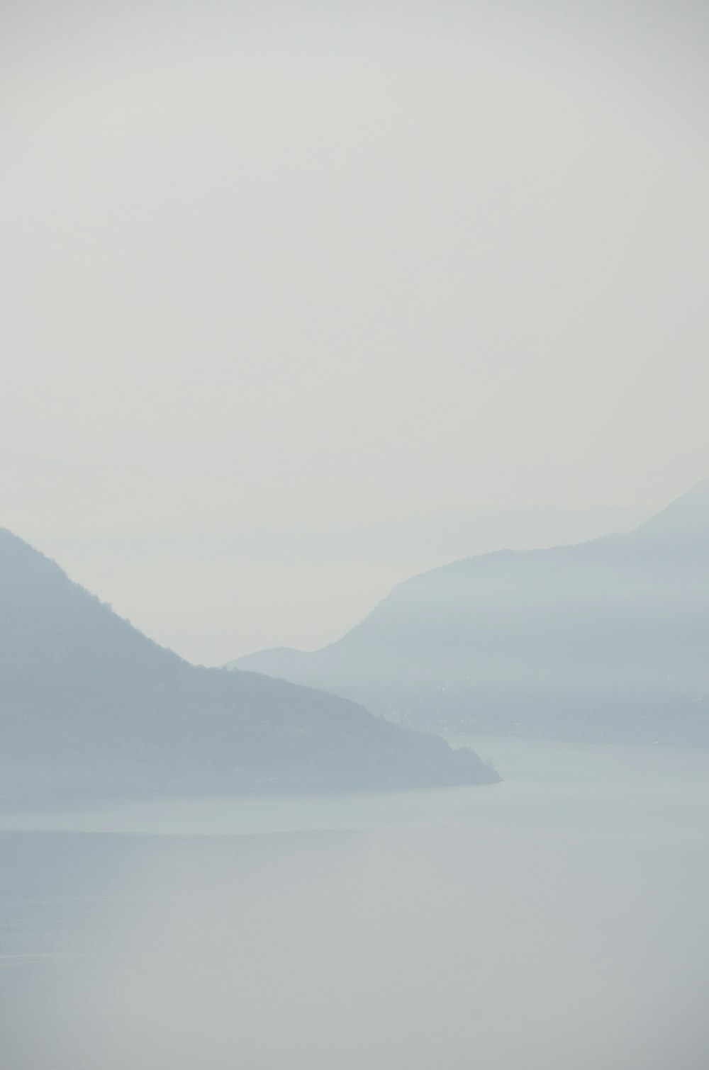 a foggy day over a lake with mountains in the distance