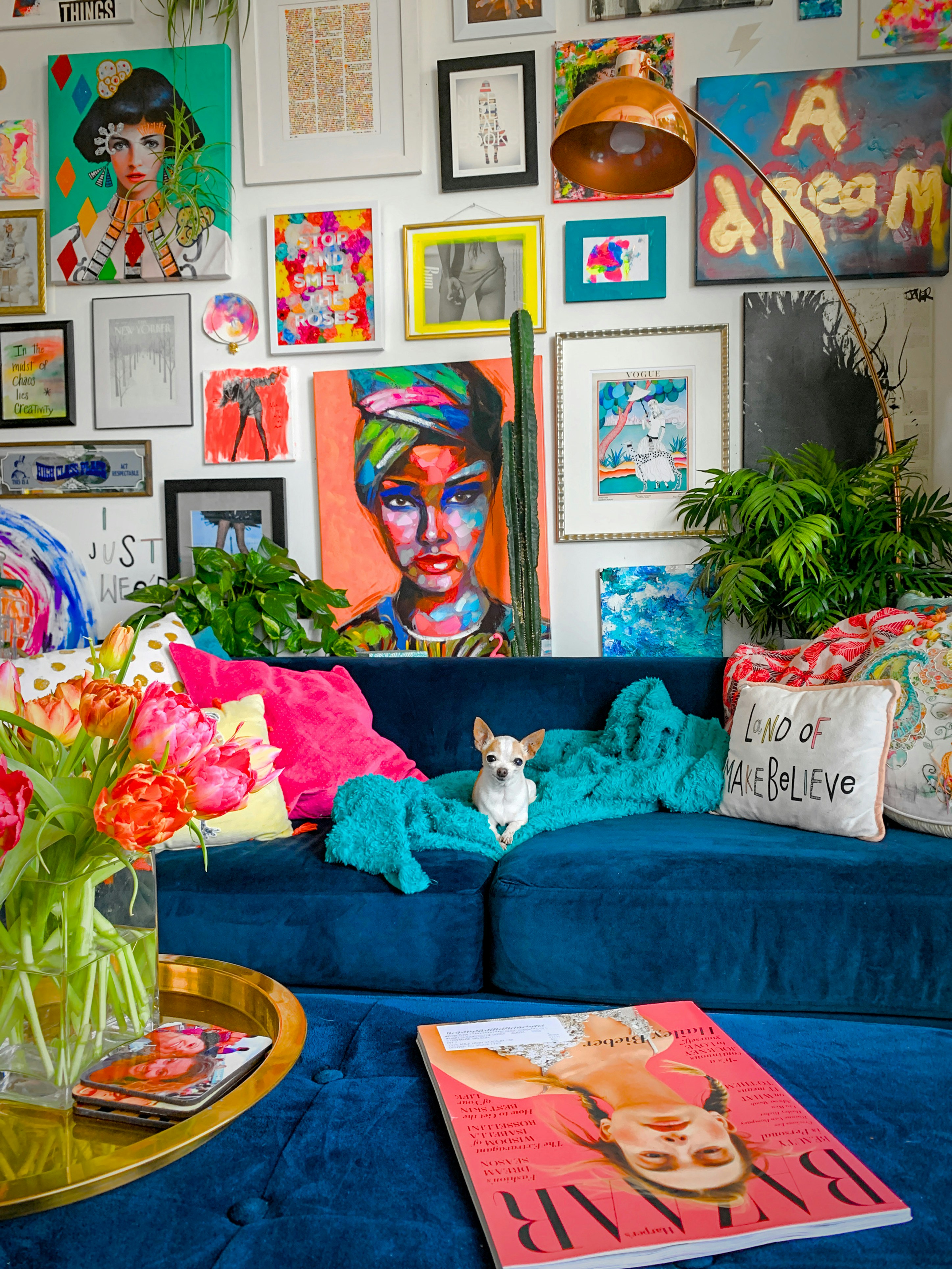 Tiny chihuahua named Gidget poses on a blue velvet couch in front of a colorful maximalist gallery wall in a Denver apartment home