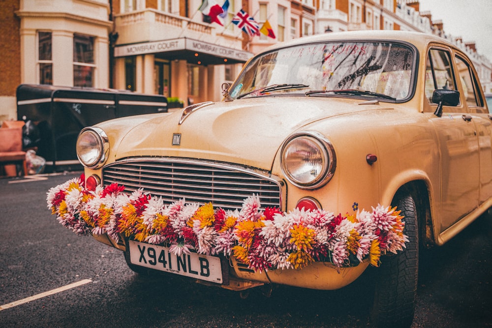 an old yellow car with a bunch of flowers on the front