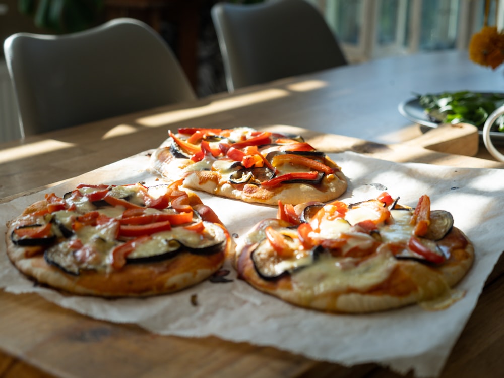 a wooden table topped with four pizzas covered in toppings