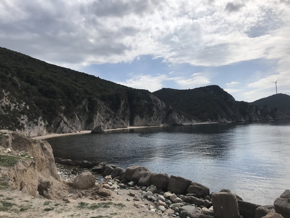 a body of water surrounded by mountains under a cloudy sky