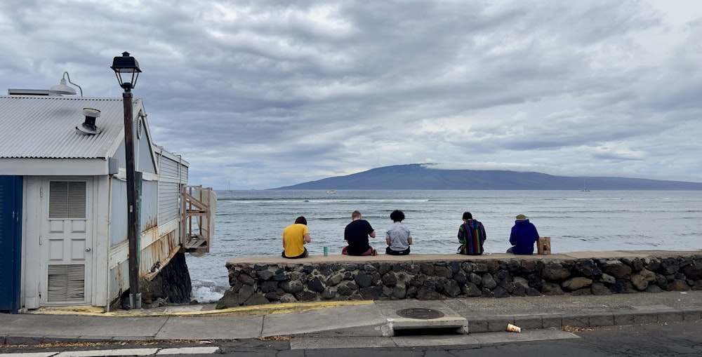 a group of people sitting on top of a stone wall next to the ocean