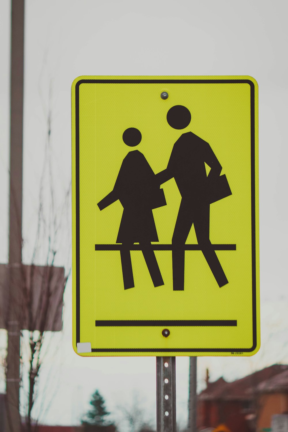 a yellow pedestrian crossing sign sitting on the side of a road