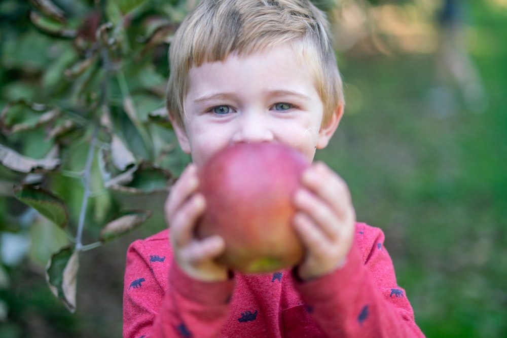 a young boy holding an apple in front of his face