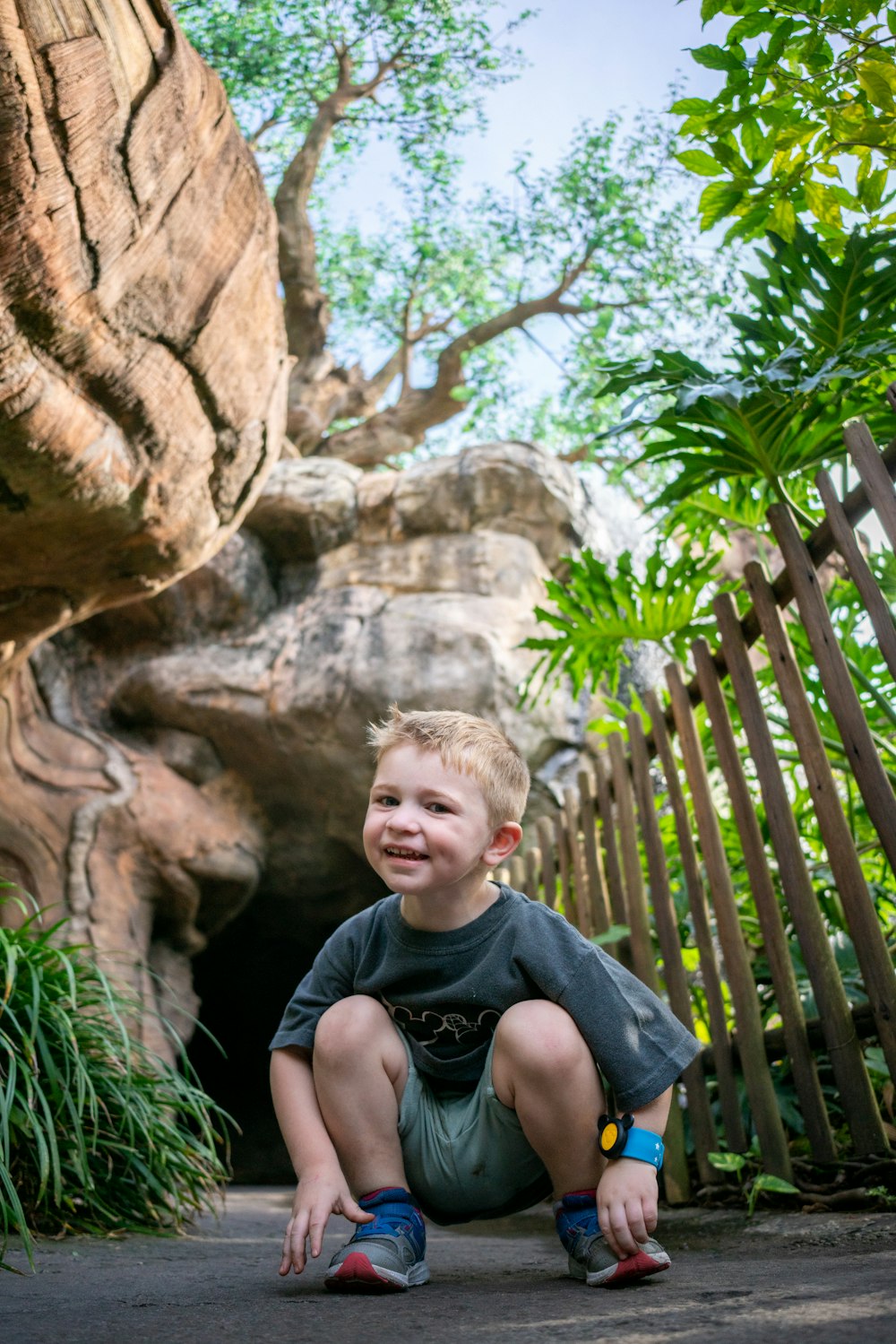 a young boy sitting on the ground in front of a tree