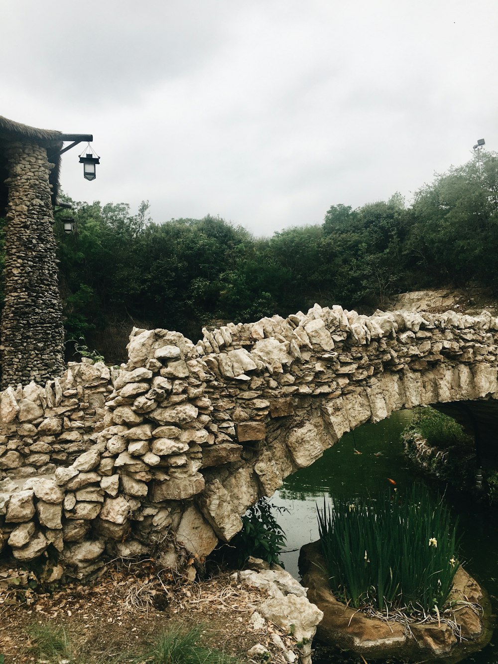 a stone bridge over a small pond in a park