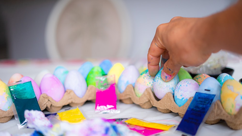 a person is putting colored eggs in a carton