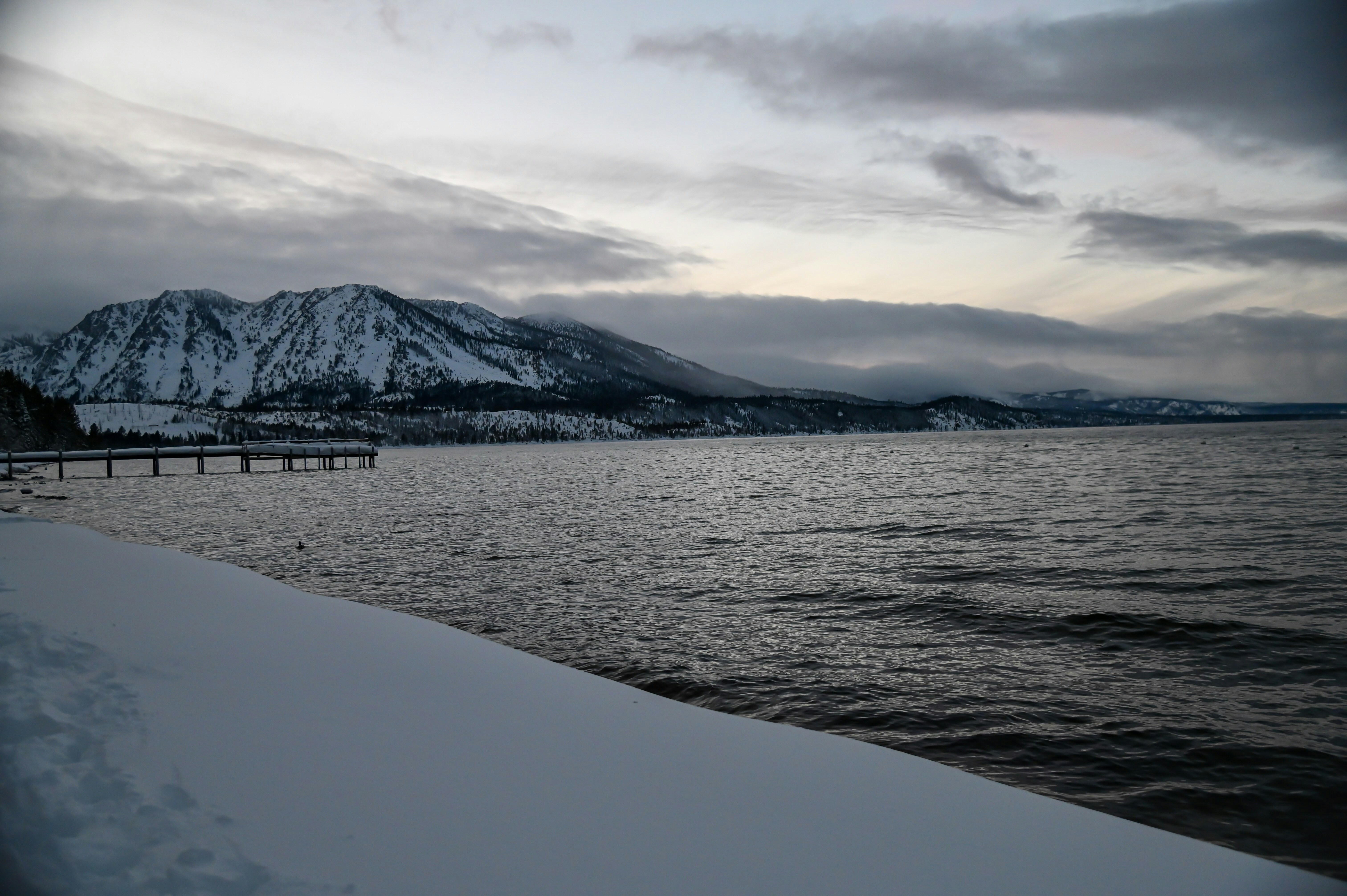 a body of water surrounded by snow covered mountains, Lake with snowy mountain in the background during winter