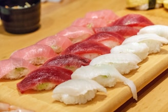 An assortment of sushi neatly arranged on a wooden serving board, featuring pieces with different types of fish such as tuna and white fish atop small mounds of rice. The setting suggests a clean, well-prepared presentation typical of Japanese cuisine.