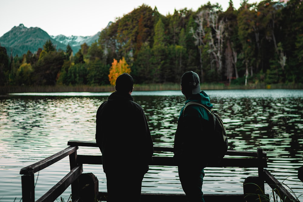 two people sitting on a bench looking at a lake