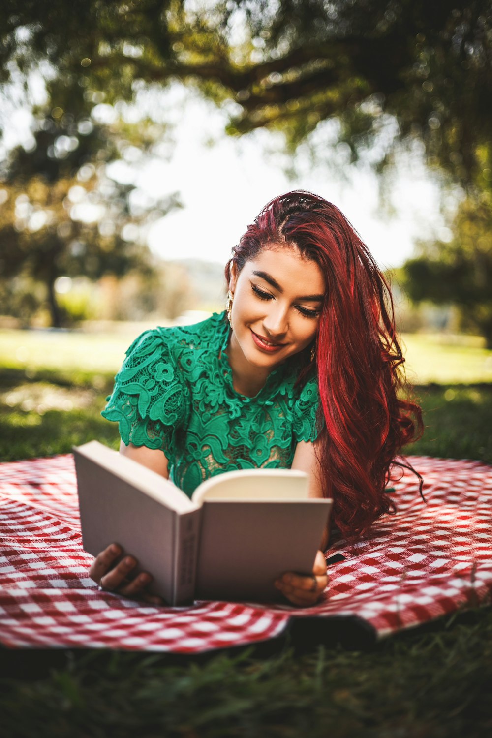 a woman laying on a blanket reading a book