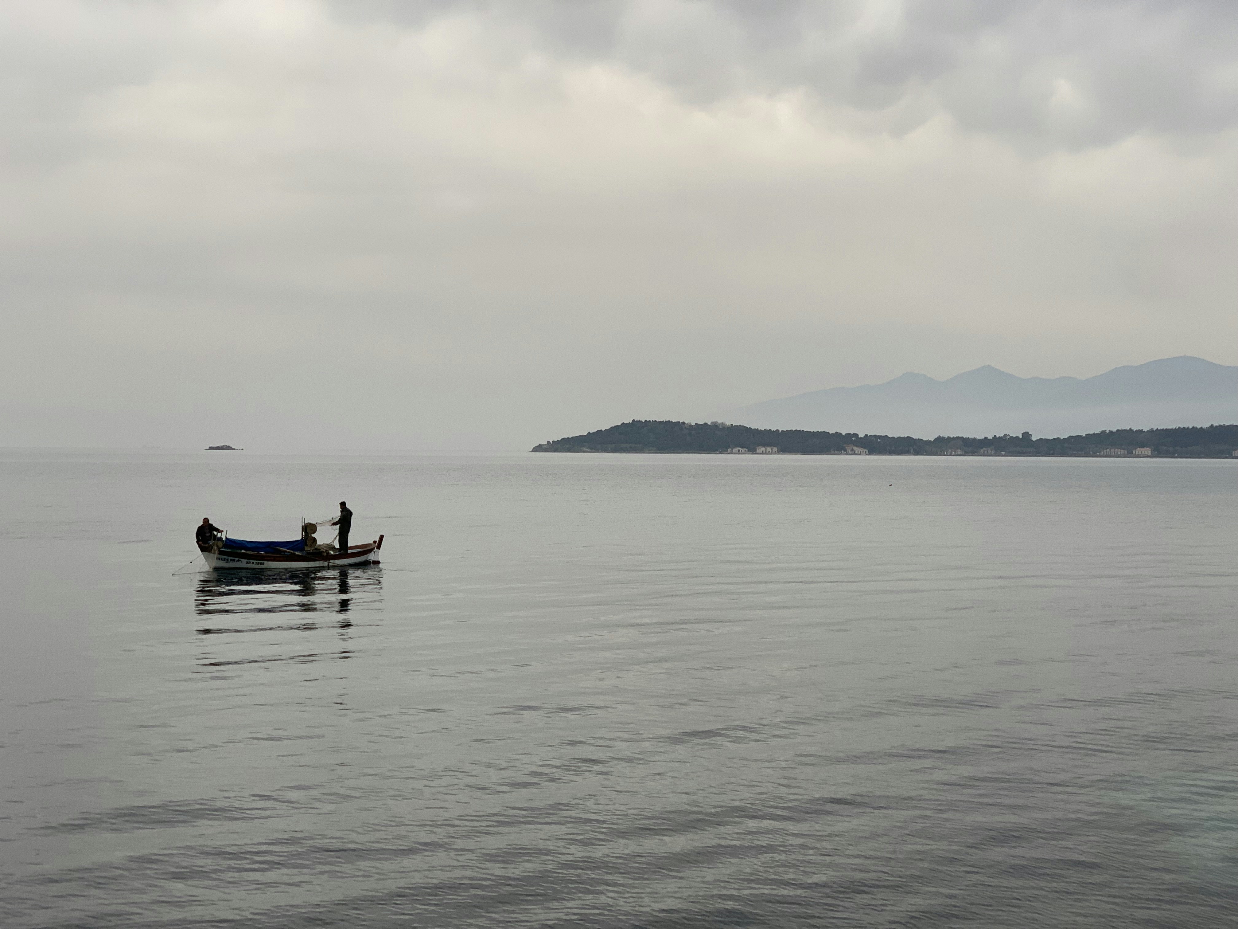 a couple of people in a small boat on a large body of water, Fishermans on a rainy day