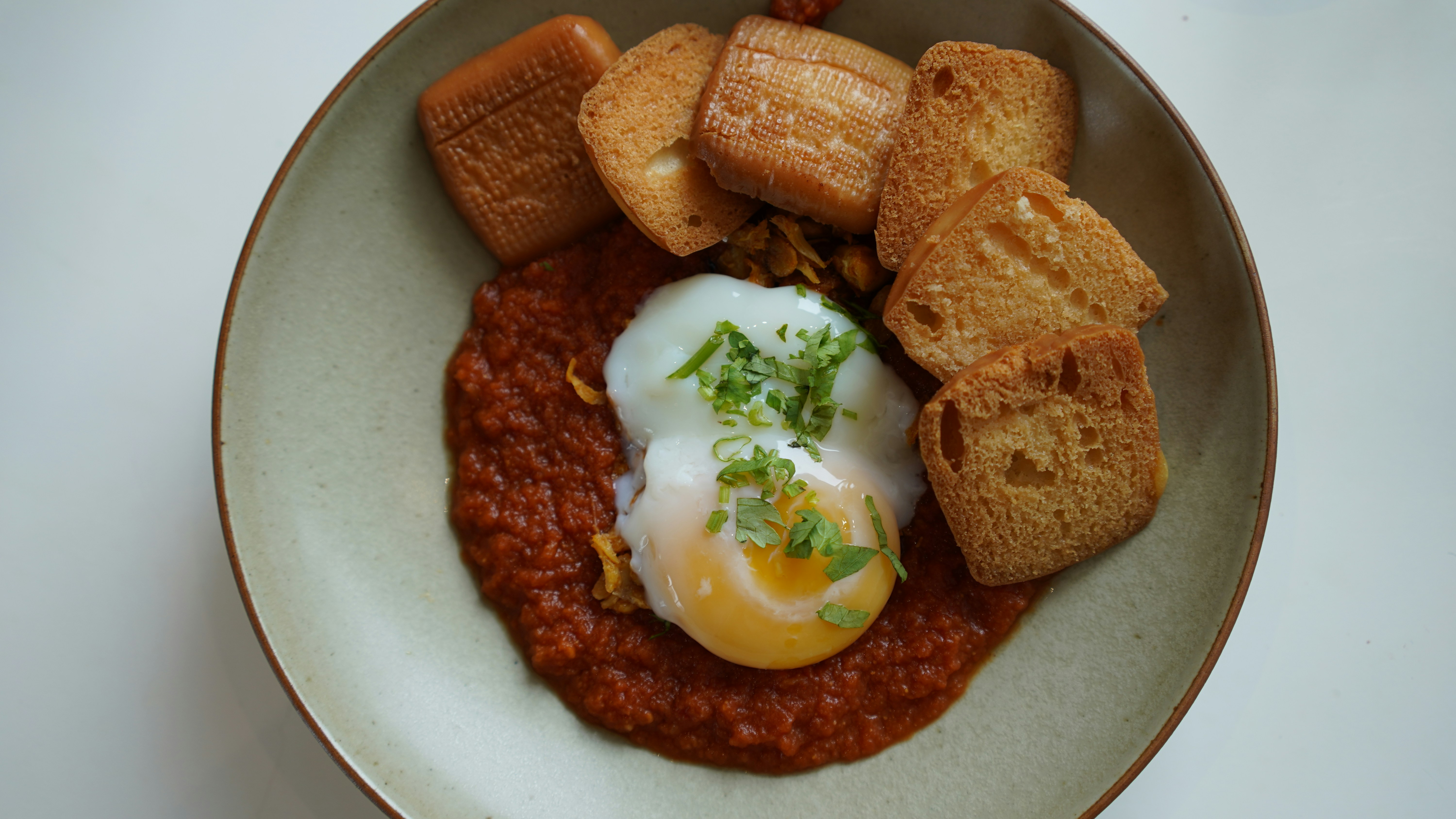 Bright red sambal chili paste being ground in a rough stone mortar with a pestle, fresh red chilies alongside