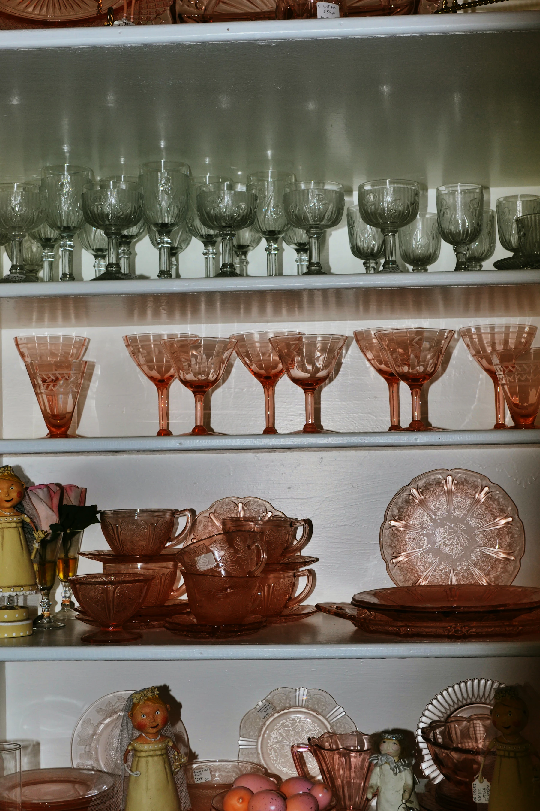 White cabinet shelves lined with pink pressed-glass goblets, cups, saucers and plates