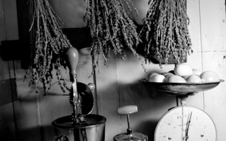 A rustic kitchen scene with dried herbs hanging from a wooden rack and a vintage scale holding several lemons. An antique manual mixer is visible on the counter, enhancing the nostalgic ambiance.