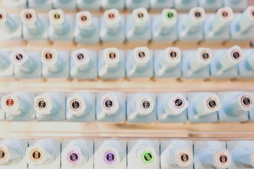 A neatly organized collection of light blue bottles with numbered labels on their tops, arranged in rows. Each bottle has a unique number, with some labels featuring a small colored circle.