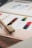 A color palette on paper with a series of vibrant paint swatches arranged in rows, accompanied by a wooden paintbrush resting on the edge. The swatches include an array of colors such as red, purple, green, and orange, neatly organized with labels.