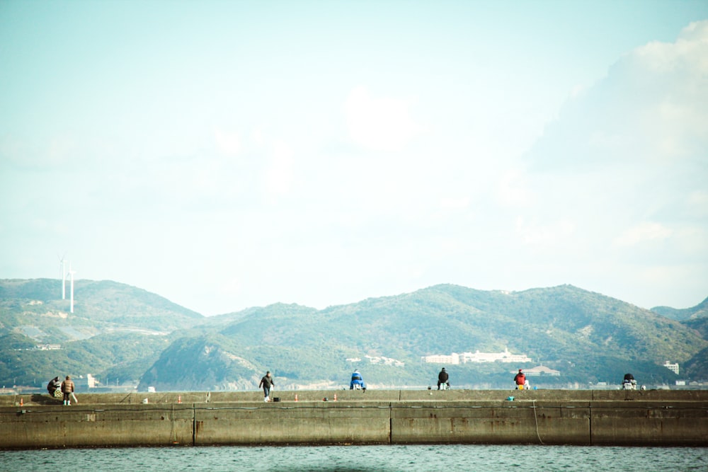 a group of people walking along a wall next to a body of water