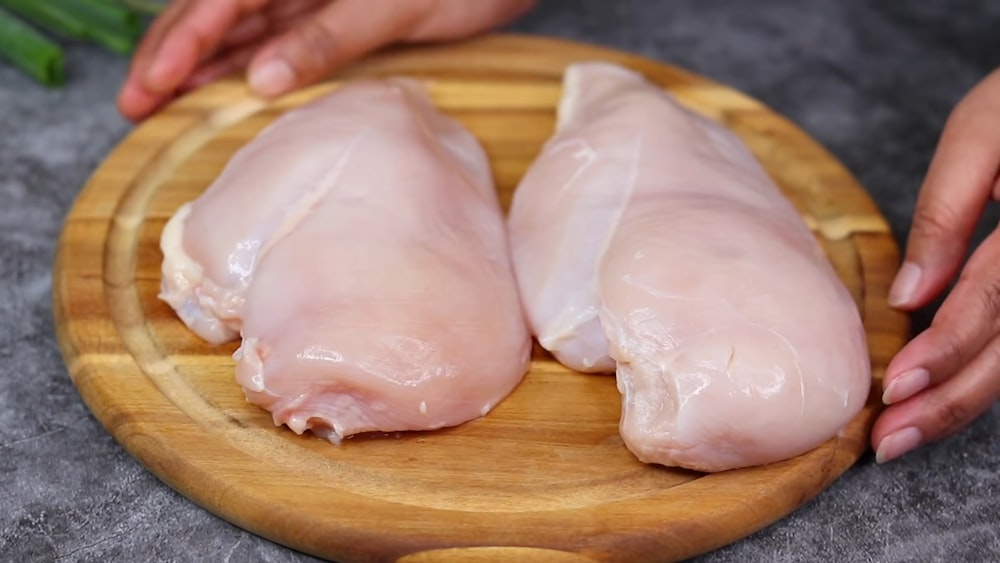 two raw chicken breasts on a wooden cutting board