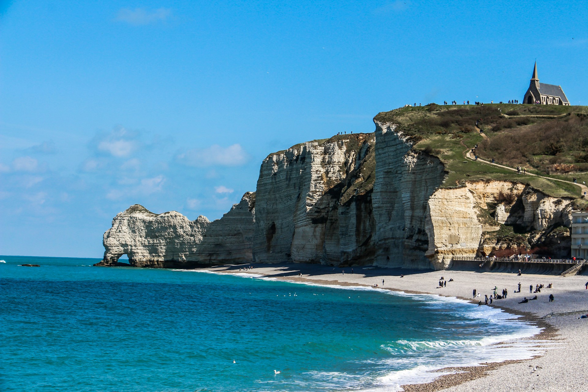 a beach with people walking on the sand and cliffs in the background