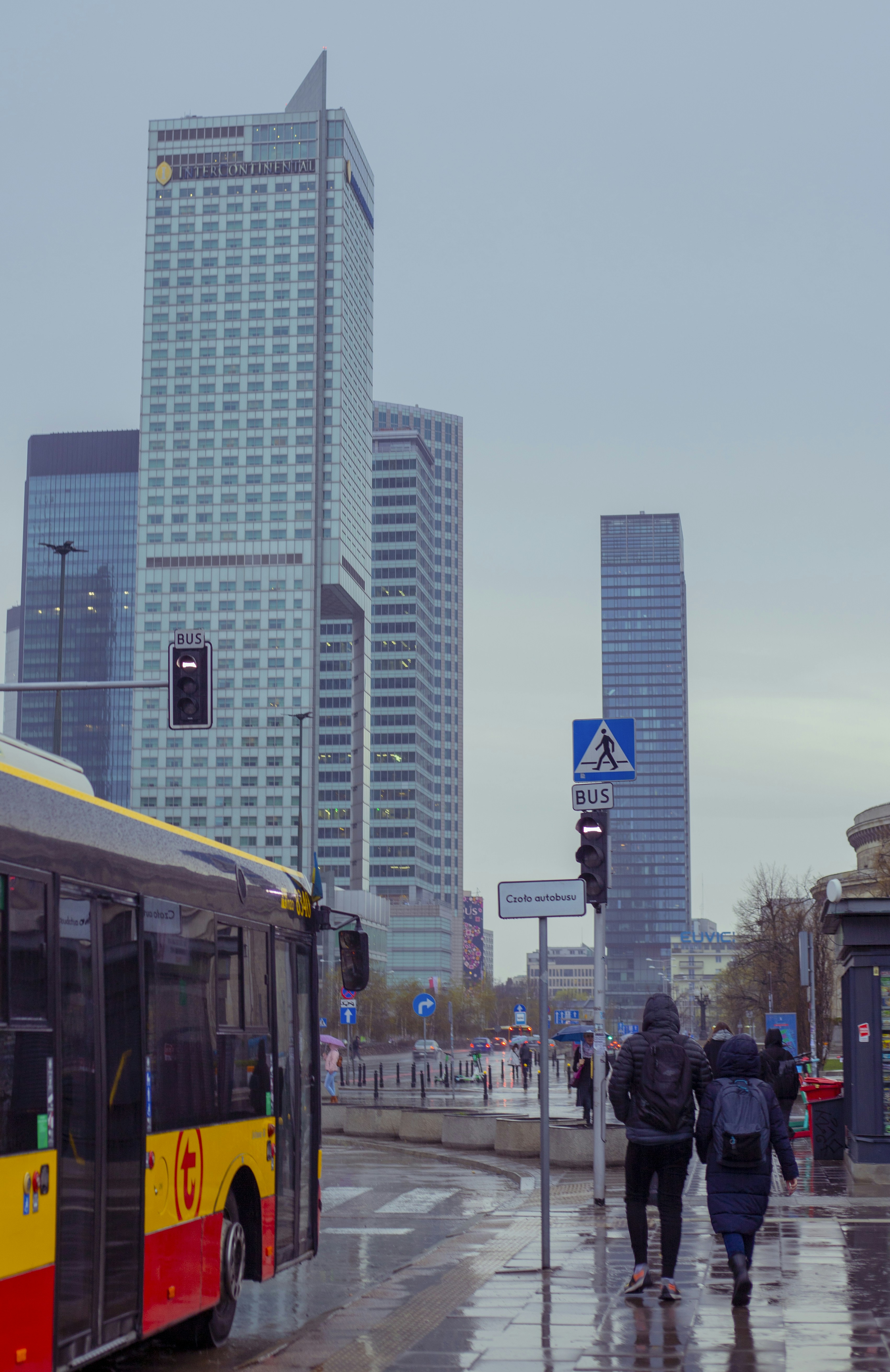 a city street with a bus and people walking in the rain