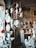 A collection of white plaster busts and sculptures displayed on shelves and a spiral staircase. Among them are various heads in classical style, some featuring hair and facial details, others more simplified. There are flowers placed on some of the sculptures, adding a touch of color. The setting appears to be an art studio or workshop with a rustic, artistic atmosphere.