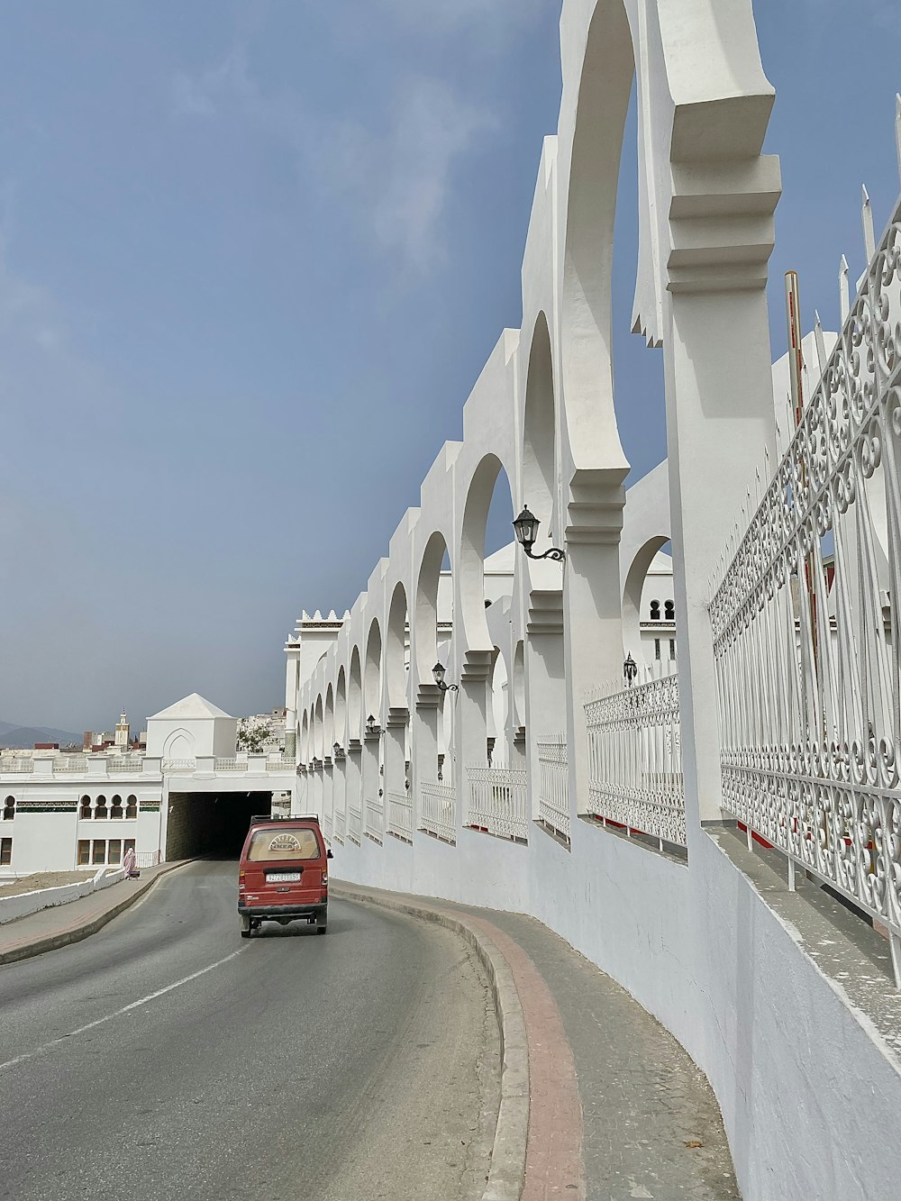 a red car driving down a street next to a white fence