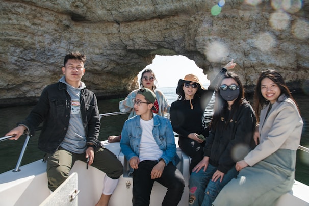 A group of friends laughing together on a boat deck, surrounded by the rocky cliffs of Capo Vaticano.