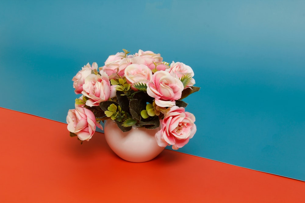 a white vase filled with pink flowers on top of a red table