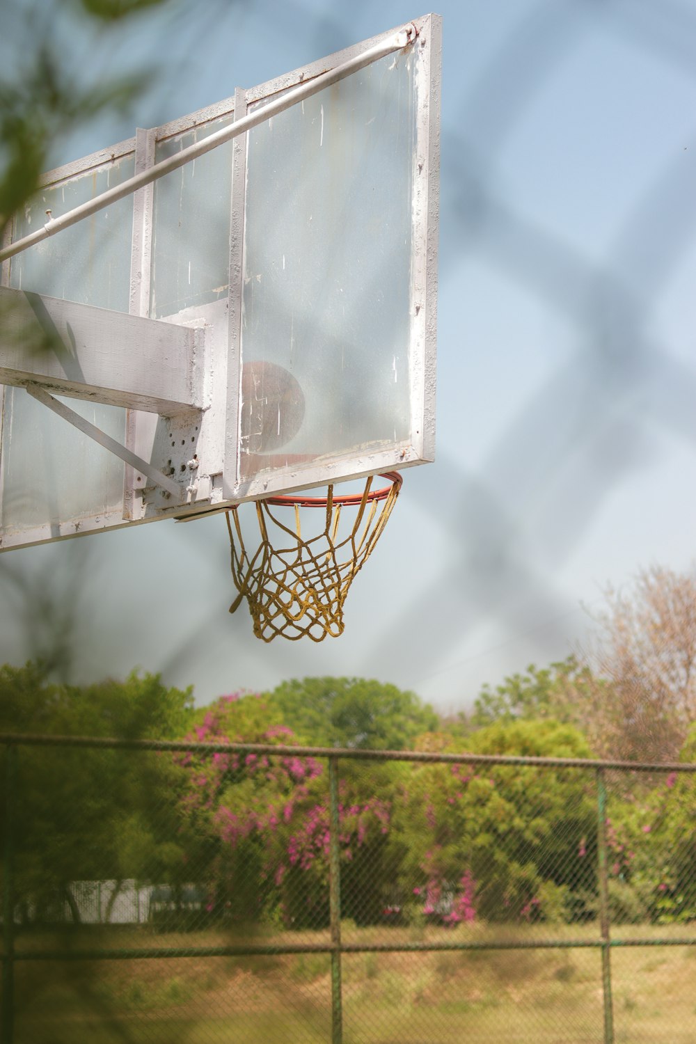 a view of a basketball hoop through a chain link fence