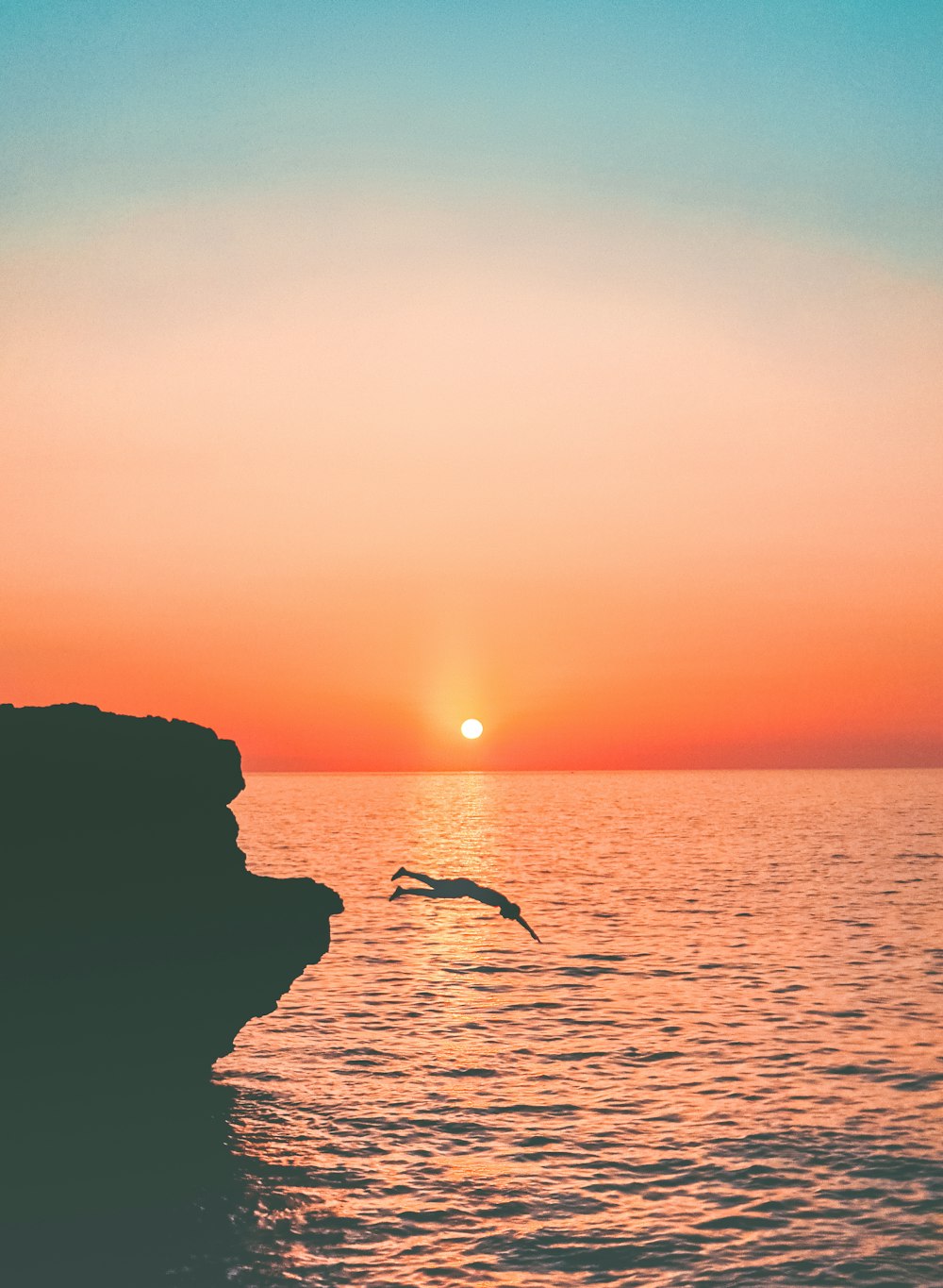 a bird flying over a body of water at sunset