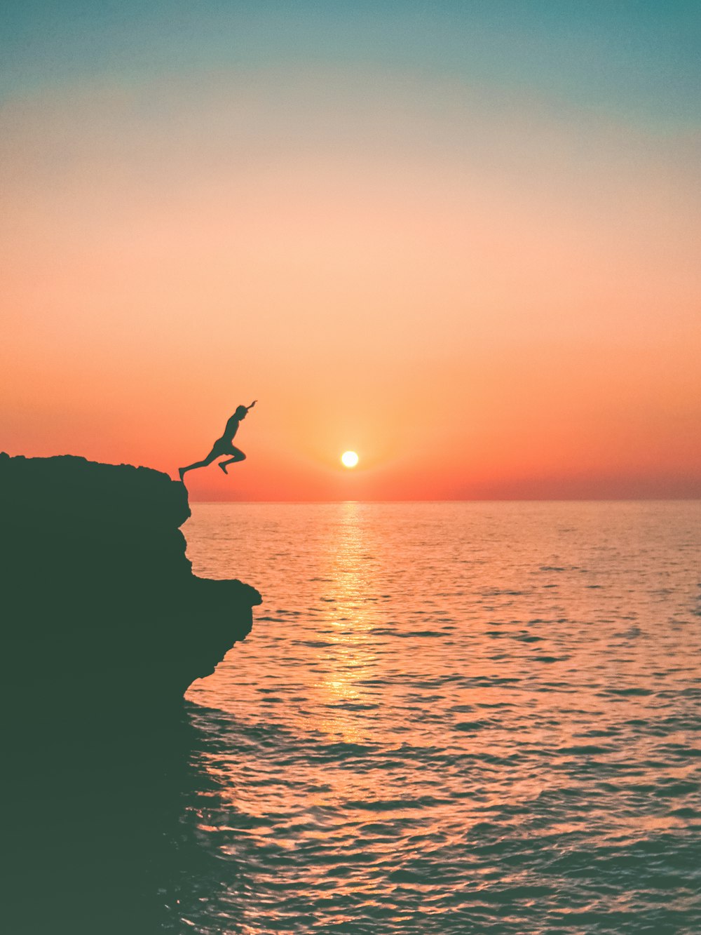 a person jumping off a cliff into the ocean